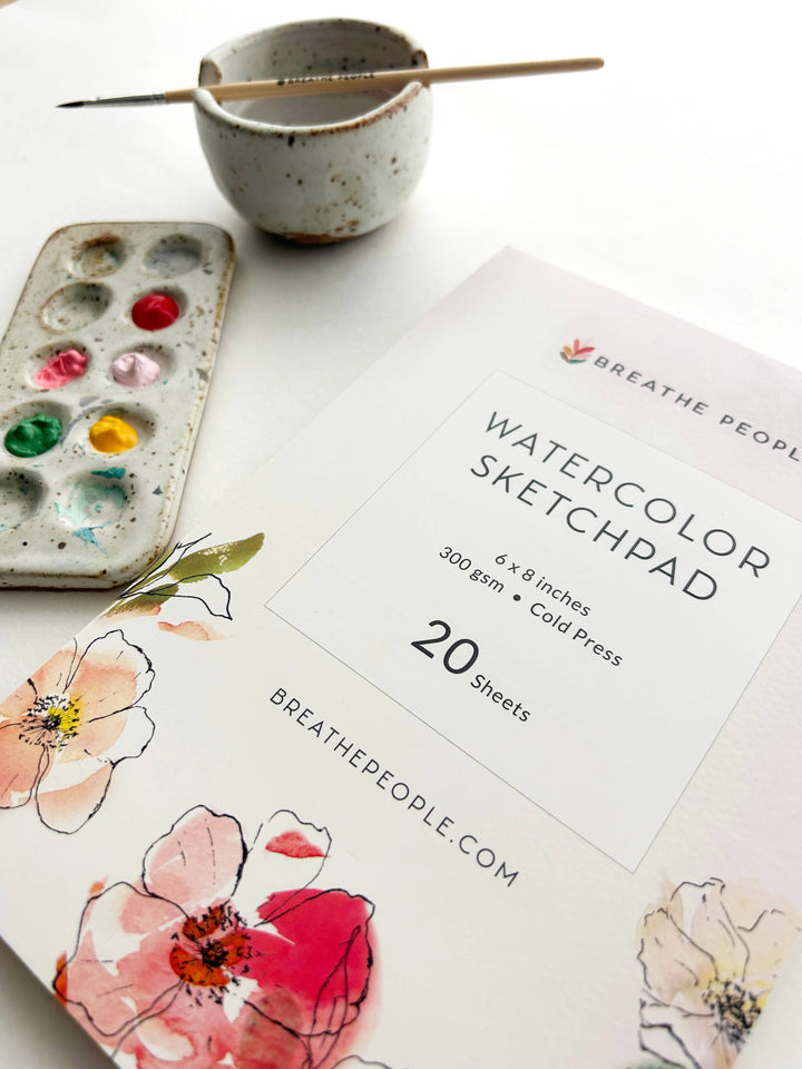 Watercolor sketchpad with floral designs, watercolor set, and paintbrush
