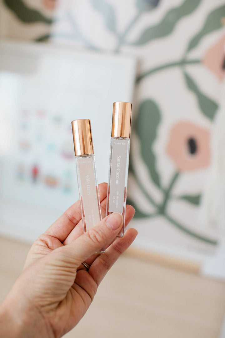 Hand holding two clear rollerball bottles with rose gold caps