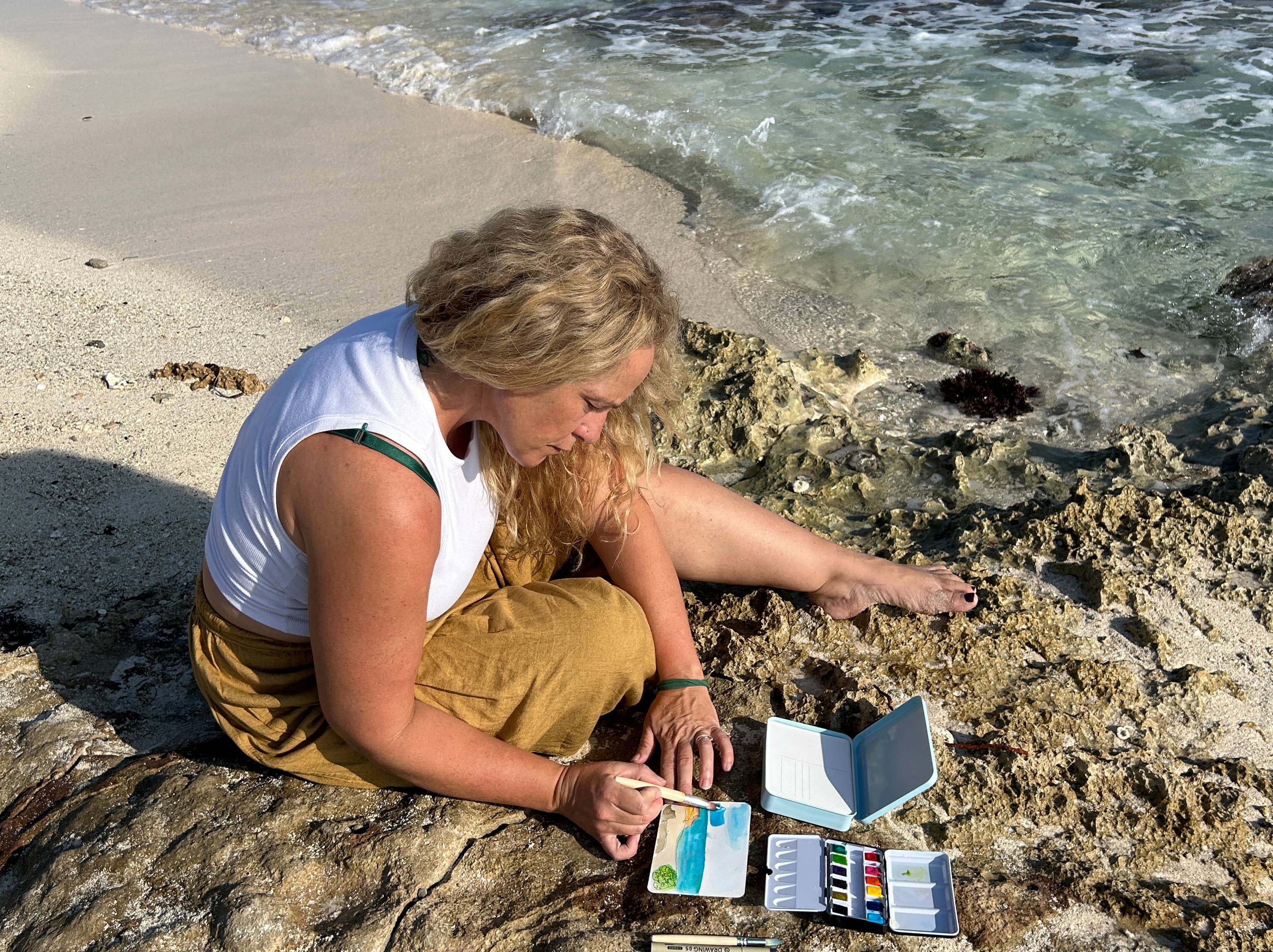 Woman painting on a rock by the ocean
