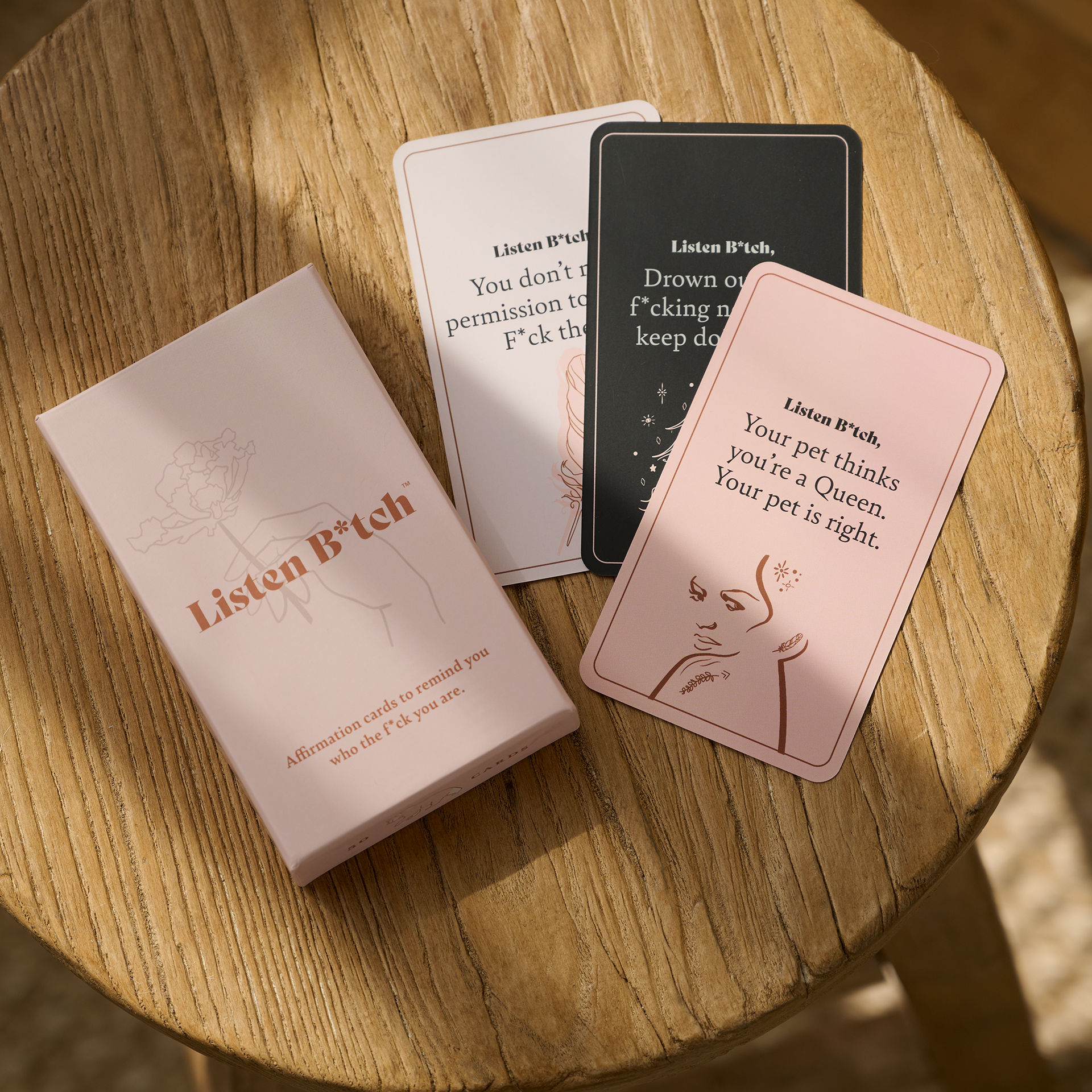 Card game 'Listen B*tch' on a wooden table with cards and packaging.