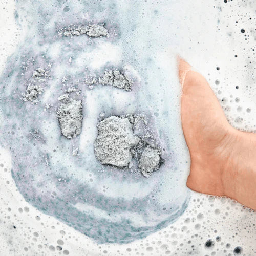 Close-up of a hand in a bath with soapy water and bubbles.