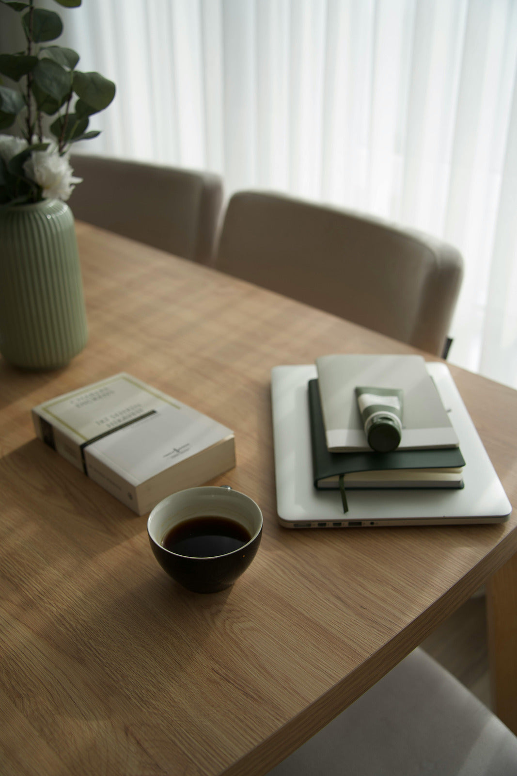 Wooden table with a cup of coffee, books, and a vase in a softly lit room.