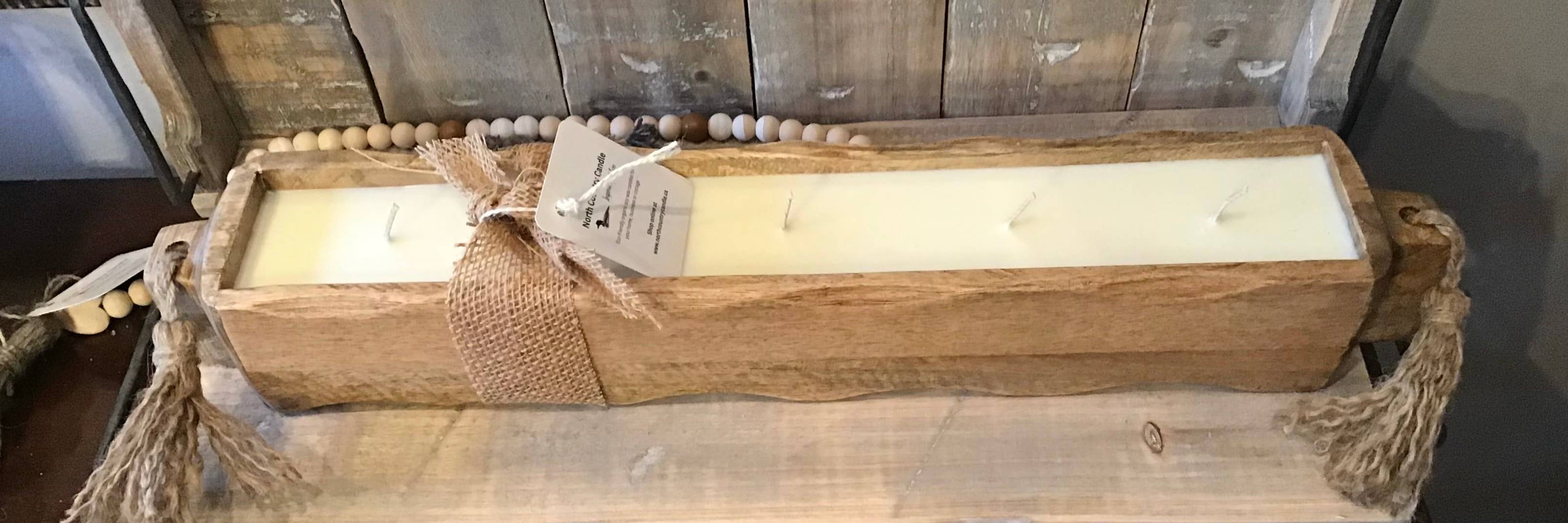 Long wooden candle holder with a candle inside, placed on a wooden surface.