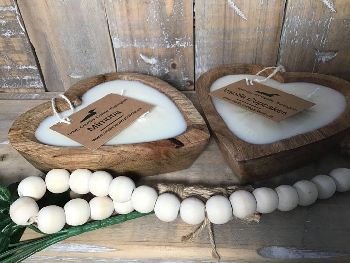 Two heart-shaped wooden candle holders with white candles and visible brand tags on a rustic wooden background.