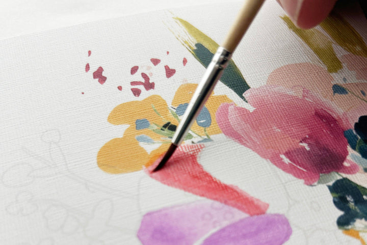 Paintbrush applying paint to a floral design on paper